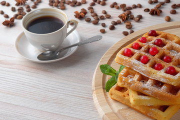 A pile of Belgian waffles with cranberries on a light cutting board and cup of black coffee and scattered coffee beans. Copy space for text.