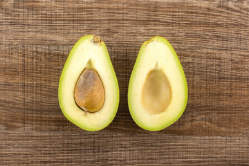 Green smooth avocado one cut in two halves table top isolated on brown wood background bacon...