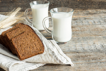 Fresh healthy milk in glass cups and sliced cereal bread on a wooden rustic background