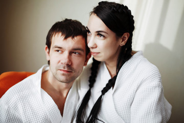 Young husband and wife of white coats play and smile in an orange armchair in a hotel room. Close up.