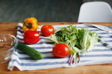 Fresh vegetables: tomatoes, green cucumber red Bulgarian pepper on a wooden kitchen table prepared for making salad.