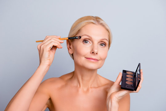 Portrait Of Charming Pretty Trendy Senior Woman Applying Eye Shadow With Brush Having Dark Palette In Hand Looking At Camera Isolated On Grey Background, Making Festive Visage