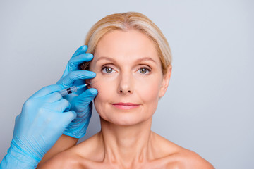 Portrait of calm serious charming aged woman with wrinkle getting injection in cheek in...