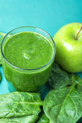 Glass with Green Fresh Smoothie from Leafy Greens Vegetables Fruits Bananas Kiwi Cucumber. Scattered Spinach Leaves Apple on Turquoise Background. Healthy Lifestyle Detox Vitamins. Copy Space