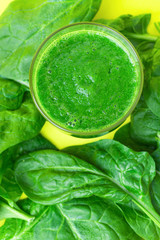 Glass with Green Fresh Smoothie from Leafy Greens Vegetables Fruits Bananas Kiwi Cucumber Apple. Scattered Spinach Leaves on Yellow Background. Healthy Lifestyle Detox Vitamins. Copy Space Top View