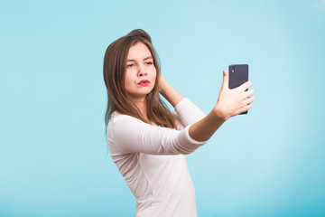 Joyful young women making selfie by her smart phone on blue background