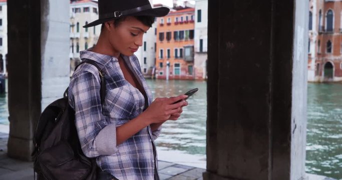 Modern young woman uses her smartphone while on vacation in Venice, Italy, Beautiful African female checks social media on her phone on her Italian vacation, 4k