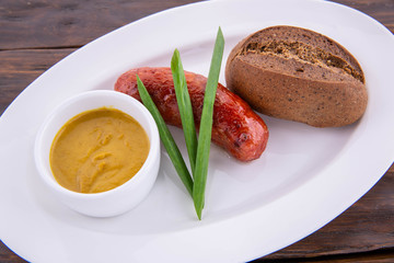 Mustard sauce, sausage from mutton, black bread, green onions on a white plate and a dark wooden background
