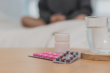 Closeup on pills and glass of water on table and Asian women sleep sick on bed in bed room