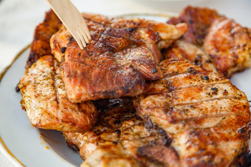 Grilled steak at the campsite lies in a white plate on the table with fork