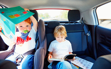 young kids sitting on back seat, reading book while traveling in the car