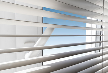 White plastic window with blinds close-up against a blue sky.