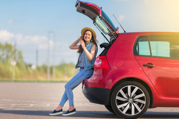 Young woman traveler sitting on hatchback car with outdoor sunny  background 
 - obrazy, fototapety, plakaty