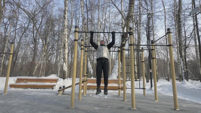 Young man doing pull up exercise on crossbar during winter gym workout