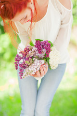 beautiful woman with red hair holding white and violet lilac bloom in her hands, outdoor garden, can be used as background