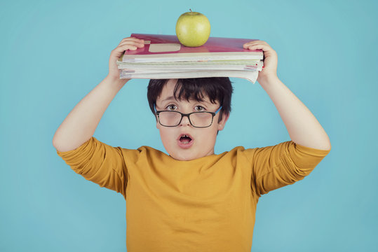niño sorprendido con libros y una manzana sobre fondo azul