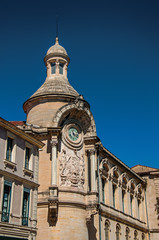 Close-up of buildings in the city center of Nimes, with clock, columns, decorative details on the walls and blue sky. Located in the Gard department, Occitanie region in southern France