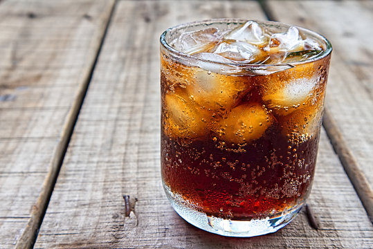 A glass of coca cola with ice on wood plate