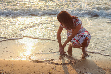 the girl on the coast paints the heart on the sand at sunrise