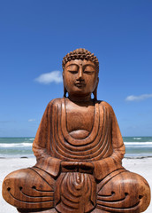 Wooden buddha statue against blue sky on beach.
