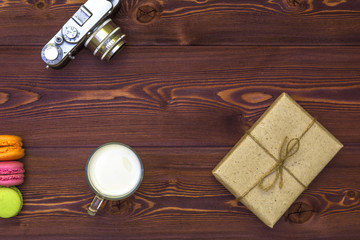 Flat lay. Retro film photocamera. Cup of milk. Cookies macaroon and Gift wrapped in paper in retro style on the table