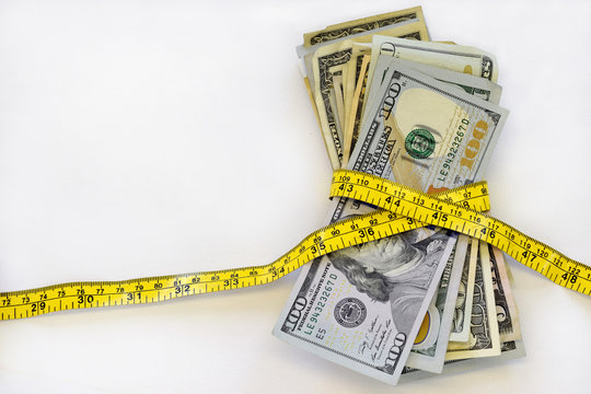Stack of cash, US dollars, with measuring tape, against white background.