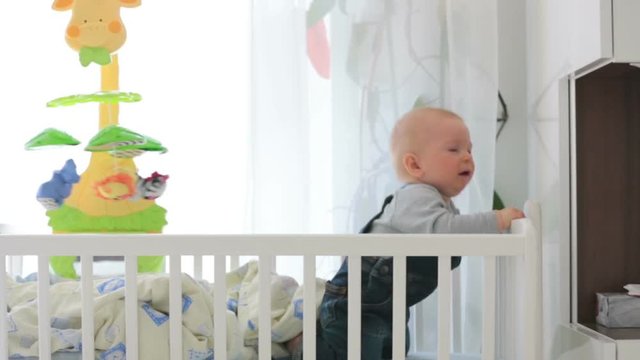 Sad baby boy, crying in crib at home