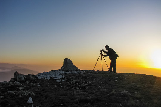 photographer takes pictures from a tripod standing on a cliff