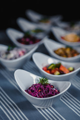 Salads in white plates on the table. Salad from beets, prunes and peanuts in the foreground. In the blurry background, there are other different salads.