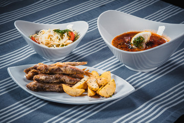 Set of three dishes. Business lunch of three dishes. Three dishes on white plates on a table with a blue tablecloth striped. Soup, salad and hot dish.