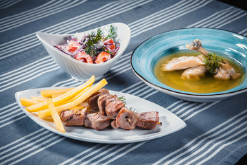 Set of three dishes. Business lunch of three dishes. Three dishes on white plates on a table with a blue tablecloth striped. Soup, salad and hot dish.
