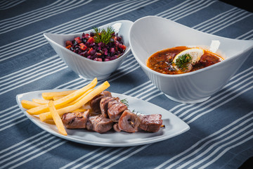Set of three dishes. Business lunch of three dishes. Three dishes on white plates on a table with a blue tablecloth striped. Soup, salad and hot dish.