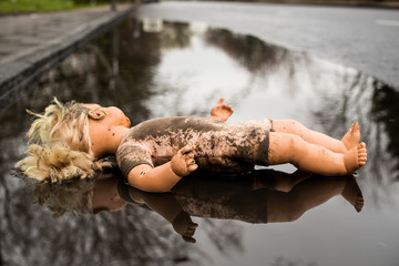 Dirty, abandoned plastic doll lying in a puddle by the roadside.