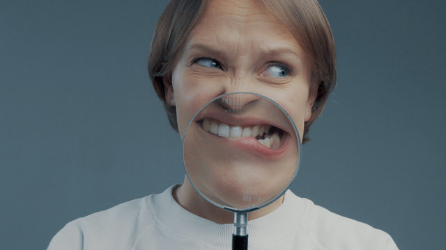 portrait of caucasian wooman with magnifier makes fun faces. Magnifier to the mouth. Woman nervious bite lips