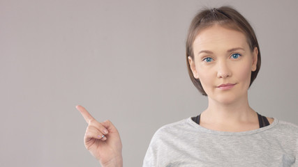 Closep portrait of midage caucasian woman on grey watching at camerashowing with finger aside on background