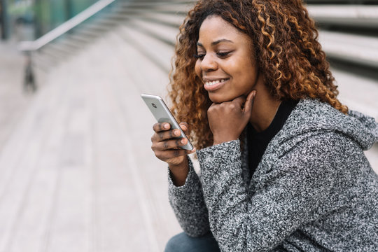 Smiling black curly-haired woman using smartphone