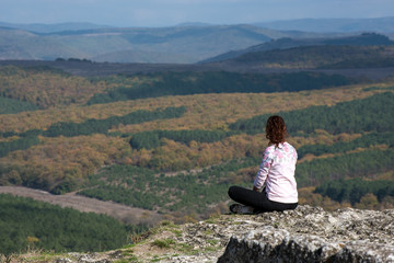 Naklejka na ściany i meble the girl sits on a cliff and looks into the distance