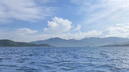 coastline of Vinperl Island, South China Sea, hills, sunlight, a small ship in the background, against the blue sky and clouds, Vietnam