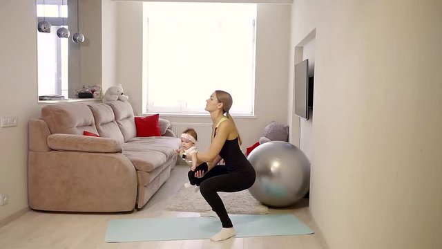 girl in sportswear performs an exercise squat with a weighting his baby