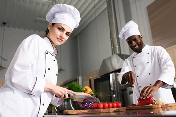 Multiracial team of cooks cutting vegetables by kitchen counter