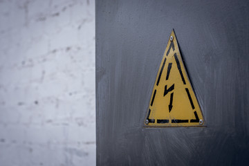 high voltage sign on a gray shield against a white brick wall