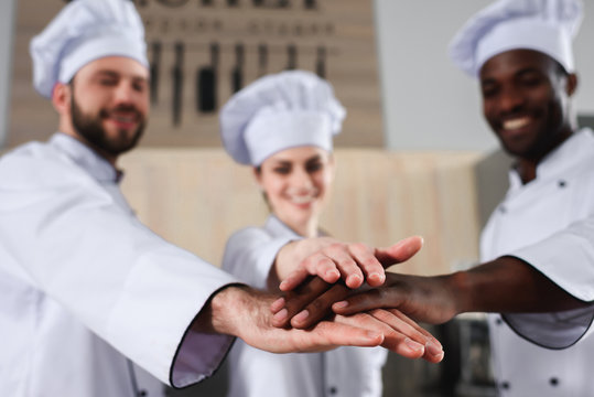Multiracial tram of cooks stacking hands together on modern kitchen