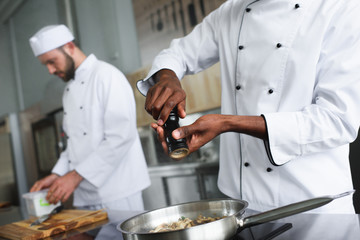 Multiracial chefs team cooking and seasoning hot dish