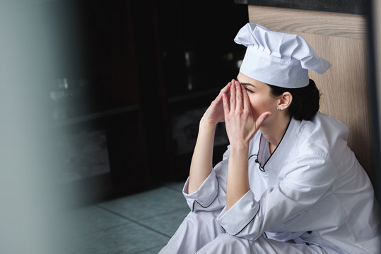 side view of chef crying and sitting on floor at restaurant kitchen