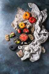 Variety of red and yellow organic tomatoes with olive oil, garlic, salt and bread for salad or bruschetta on wooden cutting board with linen cloth over blue texture background. Top view, space.