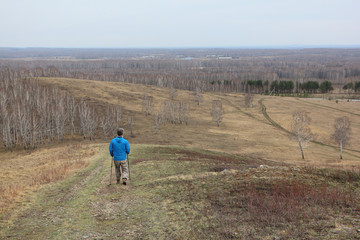 Fototapeta na wymiar Nordic Walking - adult man descending from the mountain Big, Bugotaksky hills, Novosibirsk region, Russia