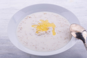 Porridge on milk with butter, is served in a white plate on a white wooden background