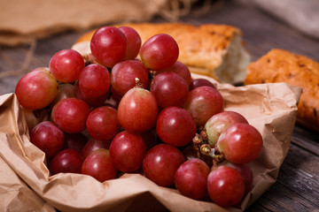 A bunch of juicy large red grapes and fresh crispy wheaten baguette on a table of dark old wooden boards
