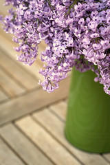 Fresh and romantic lilac in green vase on wooden background with copy space