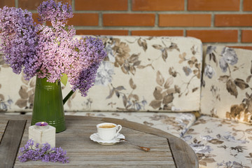 Green vase with Lilac flower, candle light and cup of porcelain coffee  on wooden table at the outdoor garden